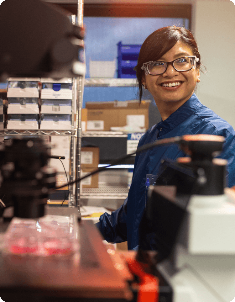 Christa Caneda stands in a lab workspace surrounded by equipment